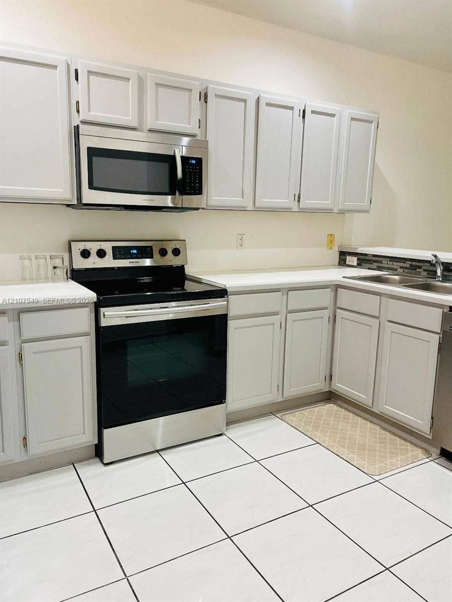 8995 NW 148th Street, #8995, Miami Lakes, Miami Lakes, FL 33018 Kitchen featuring white shaker-style cabinetry, stainless steel appliances, solid surface countertops, a mosaic tile backsplash, and ceramic tile flooring