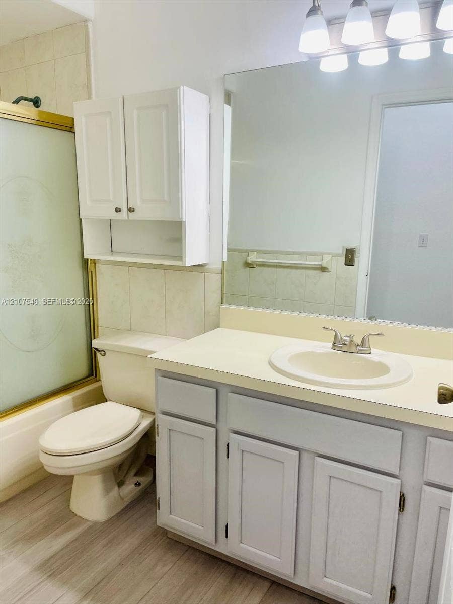 8995 NW 148th Street, #8995, Miami Lakes, Miami Lakes, FL 33018 Bathroom featuring a vanity with an integrated sink, wood-finish flooring, a wall-mounted storage cabinet, a large vanity mirror, and a tub-shower combination with a sliding glass door