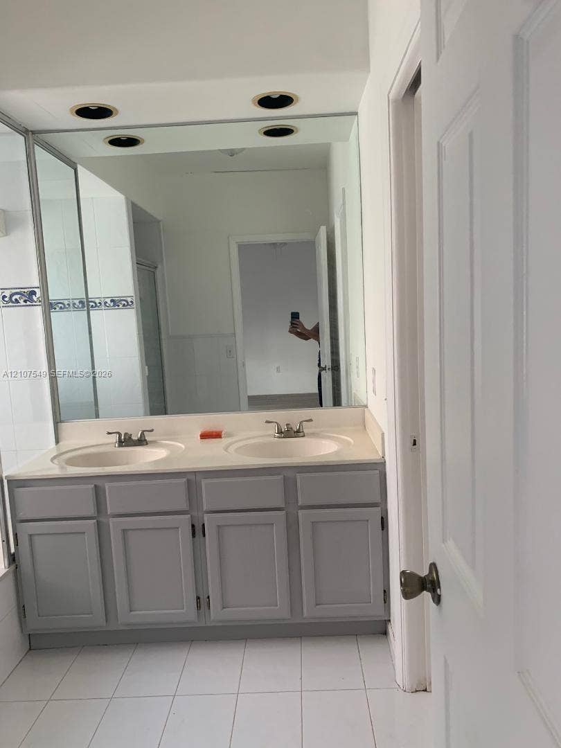 8995 NW 148th Street, #8995, Miami Lakes, Miami Lakes, FL 33018 Dual-sink vanity with gray shaker-style cabinetry, solid-surface countertop, integrated basins, and large wall-to-wall mirror with recessed lighting