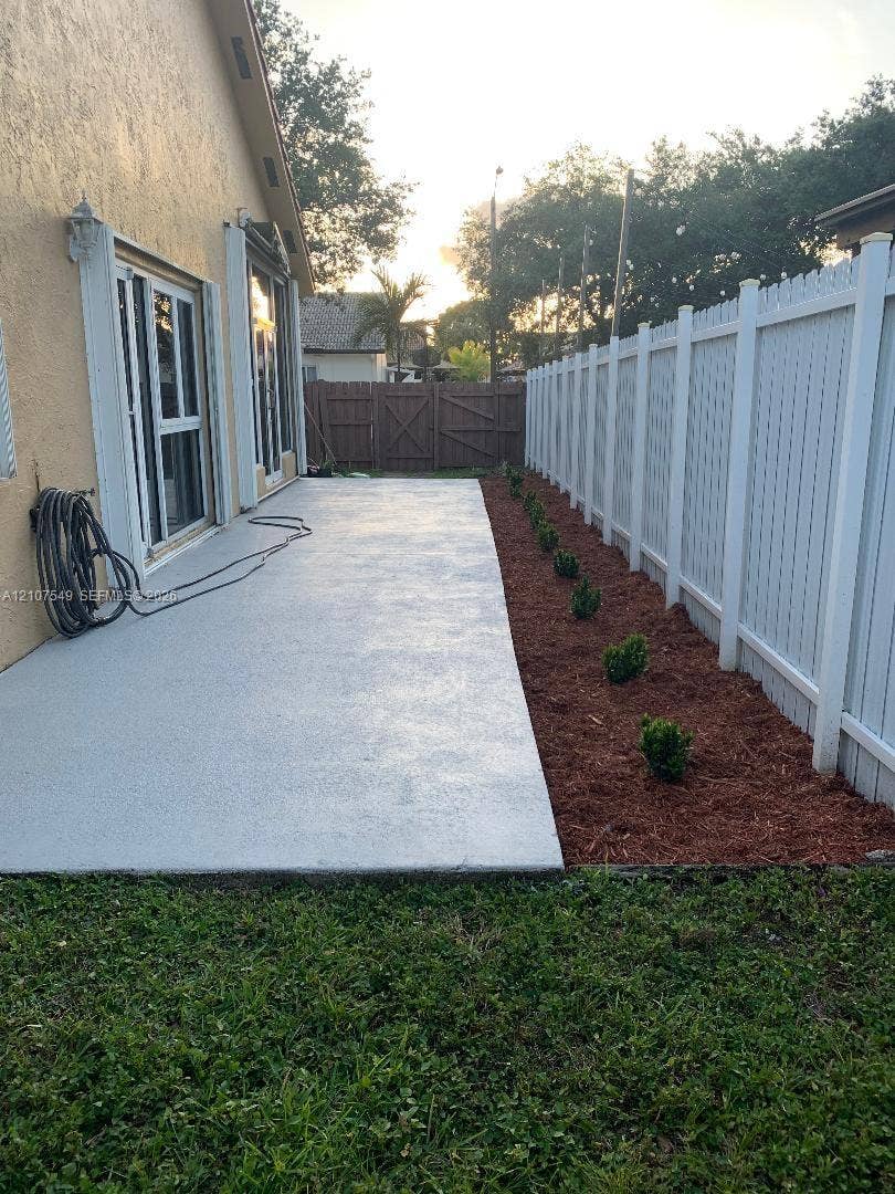 8995 NW 148th Street, #8995, Miami Lakes, Miami Lakes, FL 33018 Concrete patio featuring a white vinyl privacy fence and a mulch-lined garden border with shrubbery