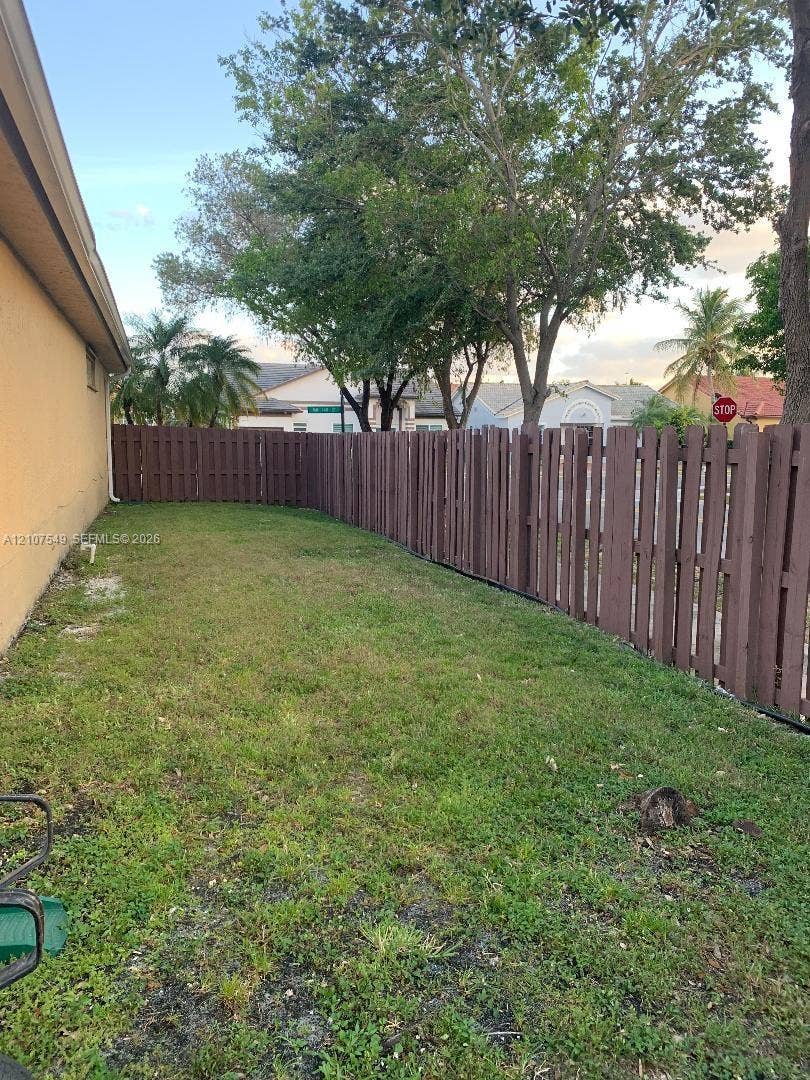 8995 NW 148th Street, #8995, Miami Lakes, Miami Lakes, FL 33018 Side yard area featuring a grass lawn enclosed by a tall stained-wood fence and mature trees