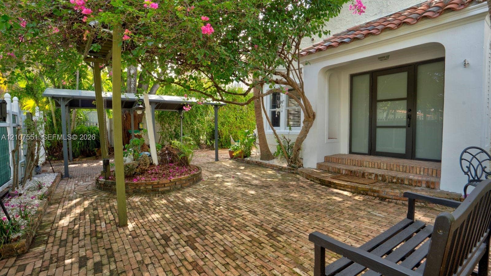 1676 SW 11th Street, Miami, Miami, FL 33135 Courtyard entry featuring a herringbone-patterned brick patio, white stucco exterior, terracotta-tiled roof accents, a covered parking structure, and a glass-paneled entry door