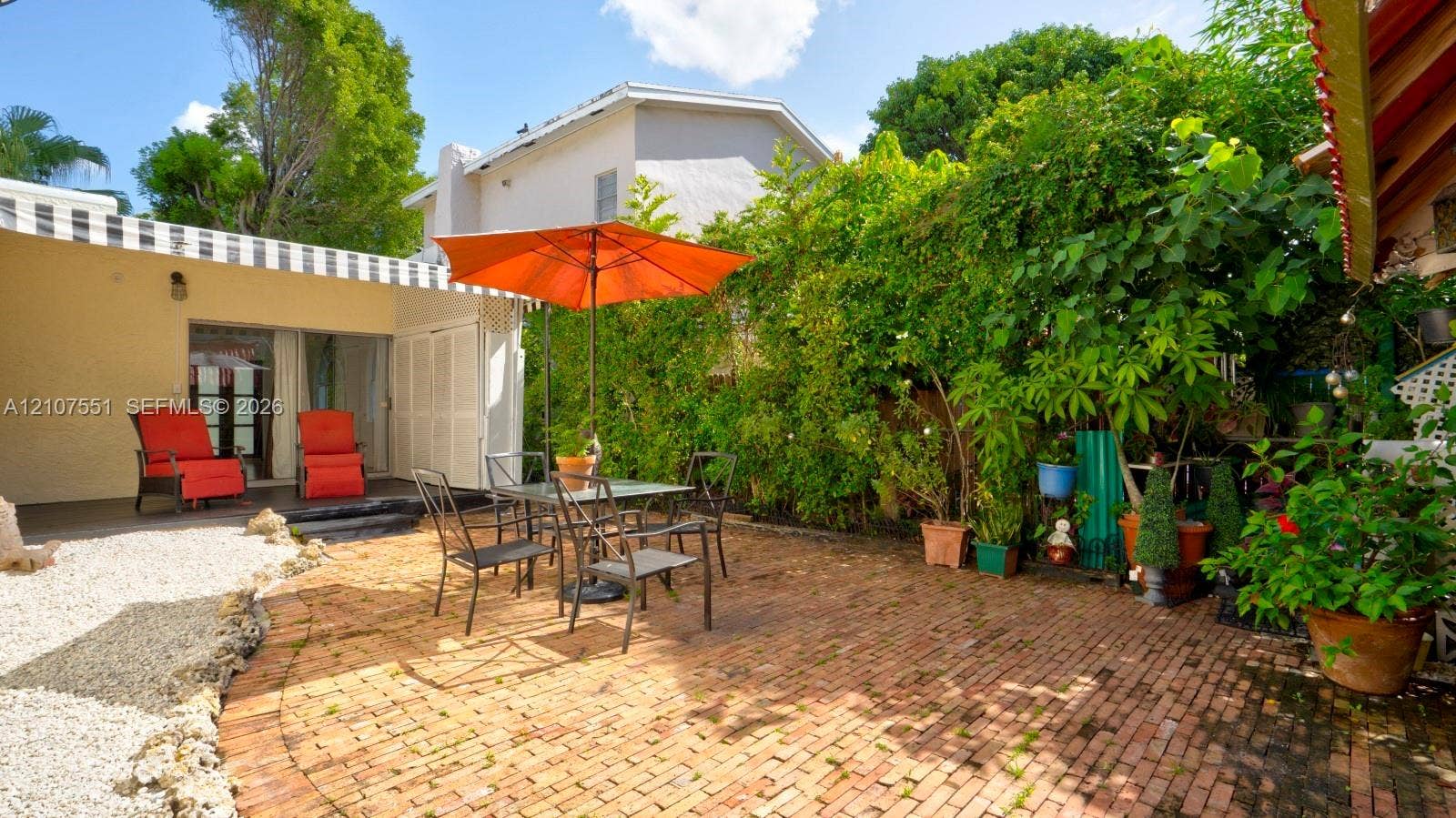 1676 SW 11th Street, Miami, Miami, FL 33135 Rear patio featuring a brick-paved surface, a black-and-white striped fixed awning, and natural foliage screening