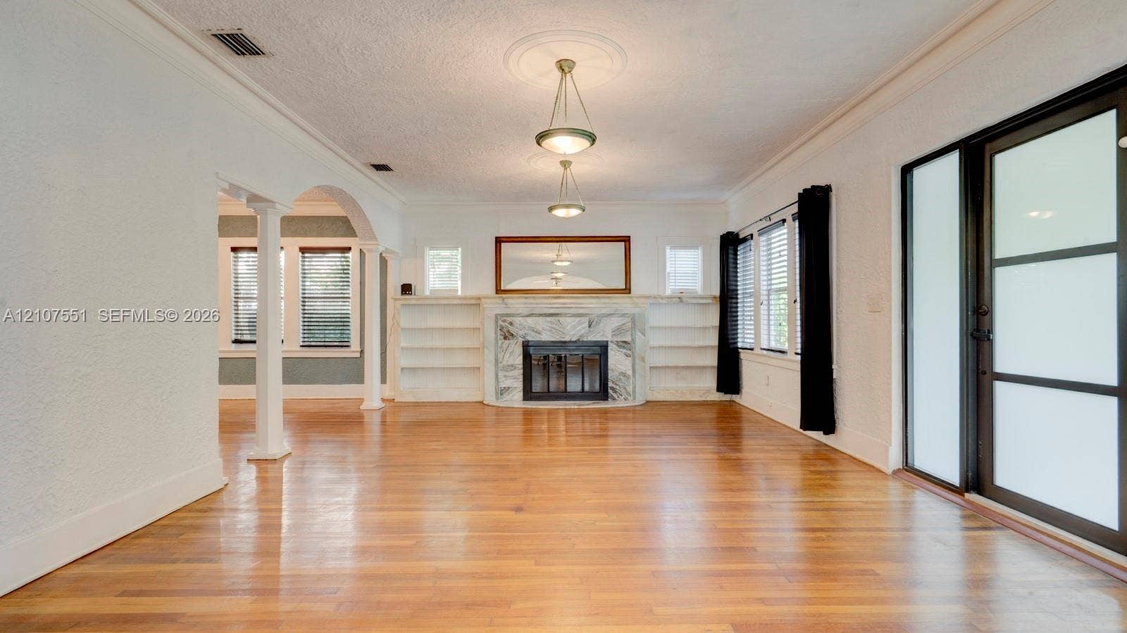 1676 SW 11th Street, Miami, Miami, FL 33135 Living area featuring wood-finish flooring, a stone-surround fireplace with built-in shelving, two hanging pendant lights with ceiling medallions, and structural columns