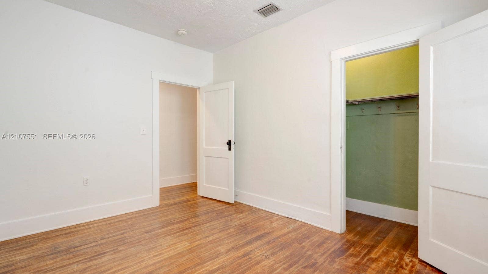 1676 SW 11th Street, Miami, Miami, FL 33135 Neutral-toned interior space featuring wood-finish flooring, two-panel interior doors with matte black hardware, and an open storage area with integrated shelving