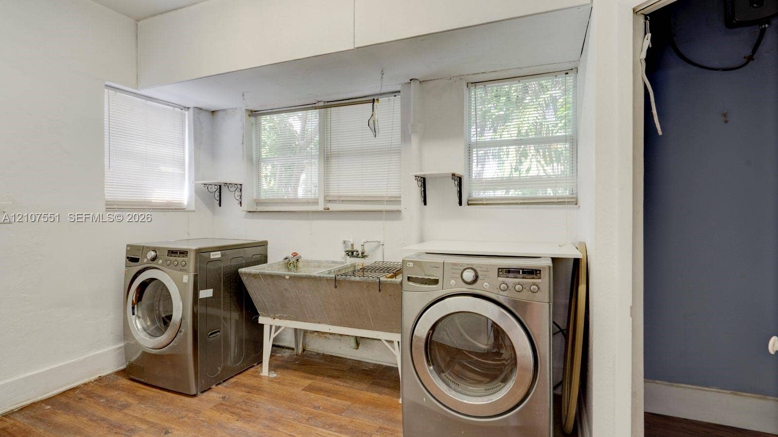 1676 SW 11th Street, Miami, Miami, FL 33135 Laundry area featuring wood-finish flooring, a freestanding stainless steel utility sink, and wall-mounted shelving