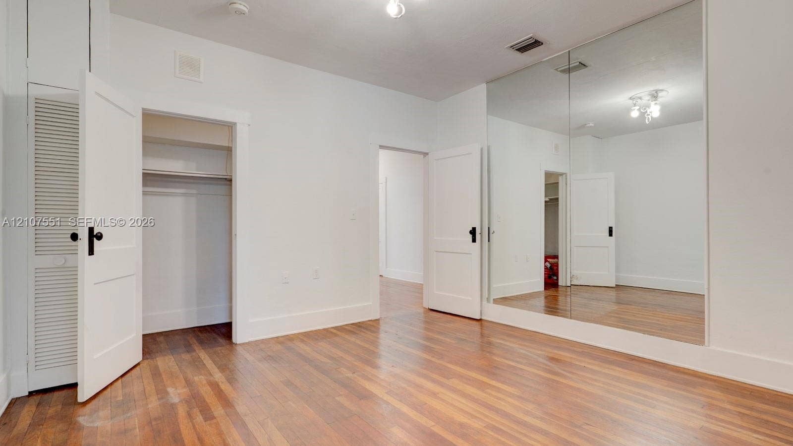 1676 SW 11th Street, Miami, Miami, FL 33135 Interior space featuring wood-finish flooring, a wall-to-wall floor-to-ceiling mirror, and solid-core panel doors with matte black hardware
