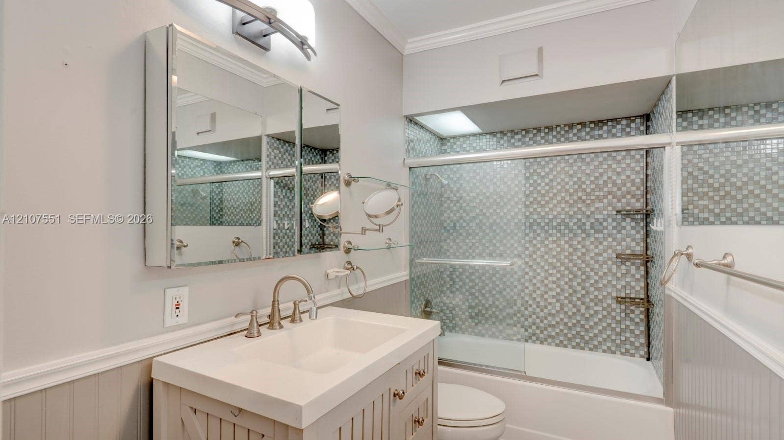 1676 SW 11th Street, Miami, Miami, FL 33135 Vanity featuring a rectangular basin, metallic faucet, and integrated storage, paired with a tri-view mirrored medicine cabinet, beadboard wainscoting, and a bathtub with mosaic tile surround and sliding glass doors