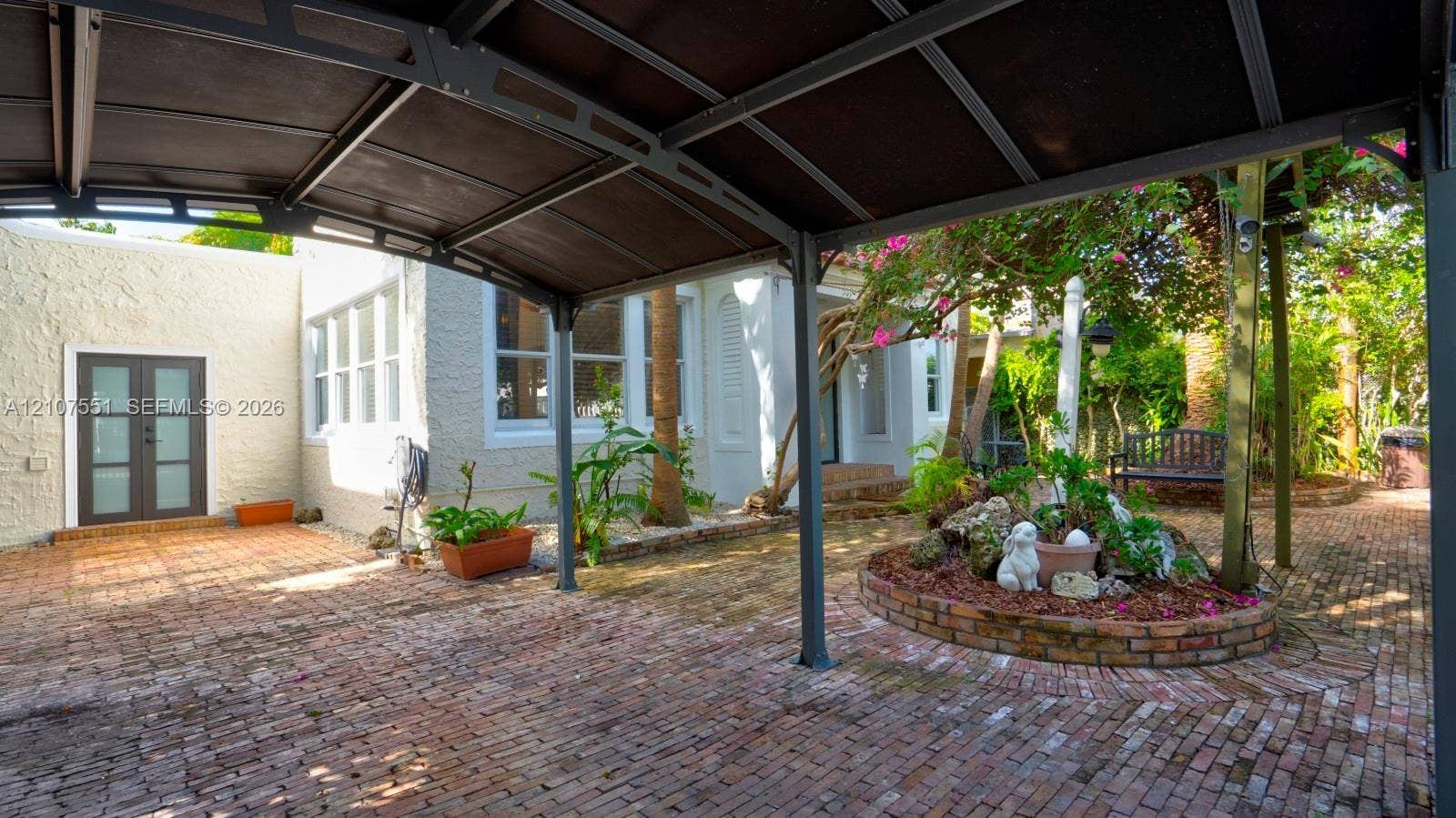 1676 SW 11th Street, Miami, Miami, FL 33135 Covered outdoor structure with dark metal frame, brick paver ground surface, and circular brick-bordered landscaping bed