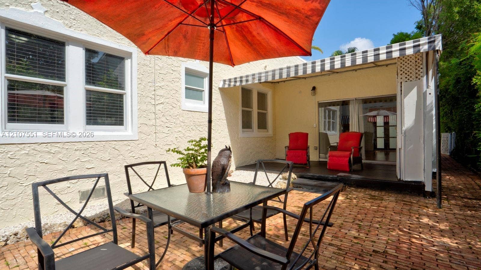 1676 SW 11th Street, Miami, Miami, FL 33135 Stucco exterior featuring a brick-paved patio, retractable striped awning, and large white-trimmed windows