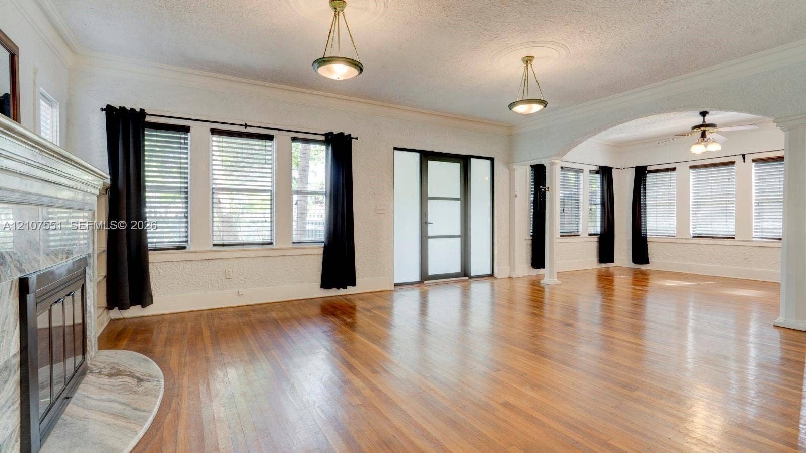 1676 SW 11th Street, Miami, Miami, FL 33135 Wood-finish flooring, stone-surround fireplace, arched architectural opening, pendant lighting with decorative ceiling medallions, and multi-pane entry door