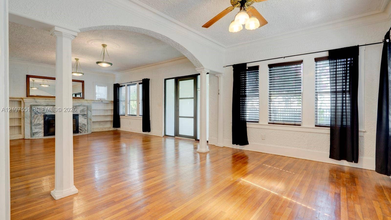 1676 SW 11th Street, Miami, Miami, FL 33135 Open living area featuring wood-finish flooring, a stone-surround fireplace, built-in shelving, decorative columns, and an arched architectural opening