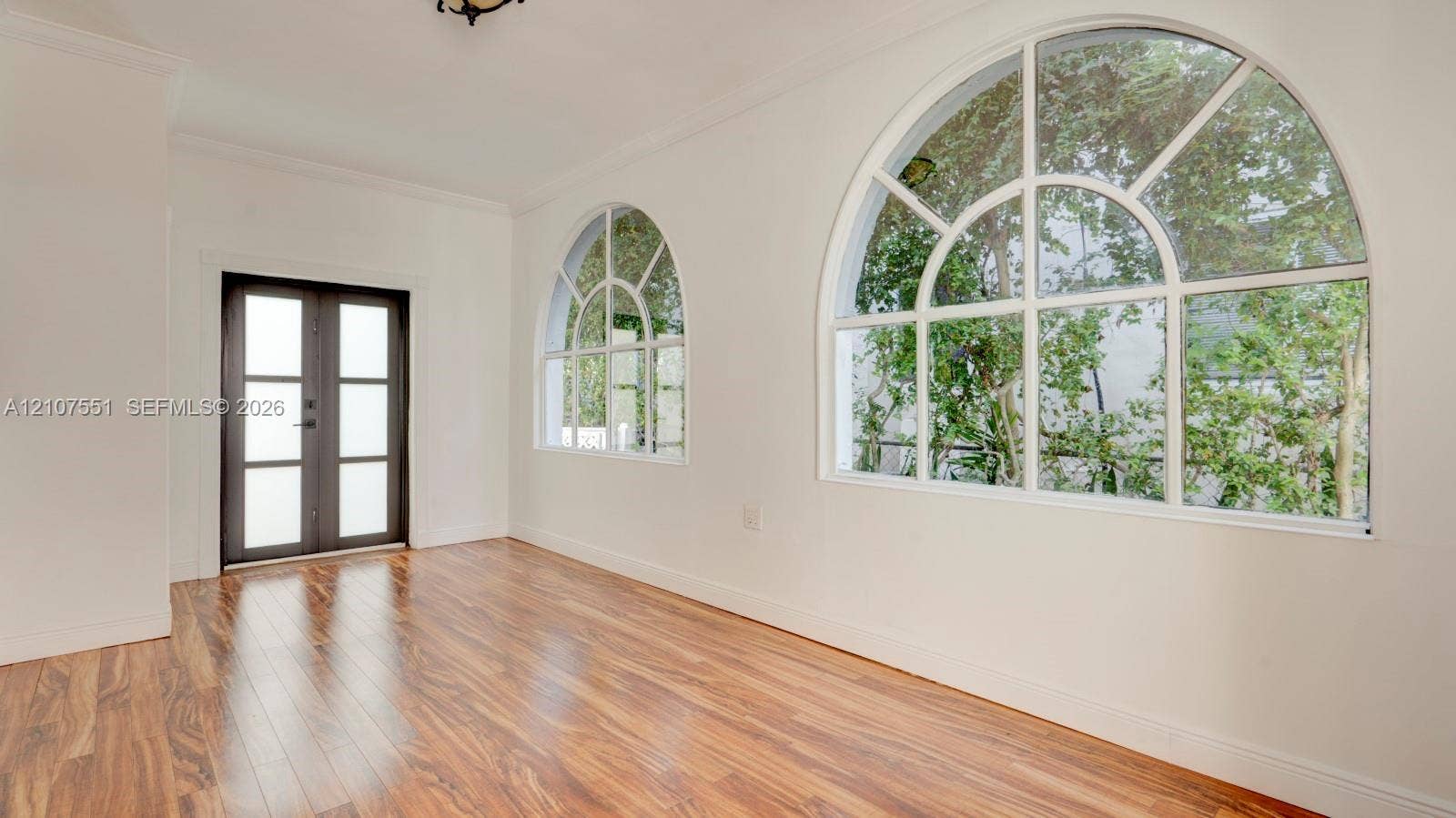 1676 SW 11th Street, Miami, Miami, FL 33135 Wood-finish flooring, two large arched windows with muntins, and a dark-framed entry door with frosted glass panes