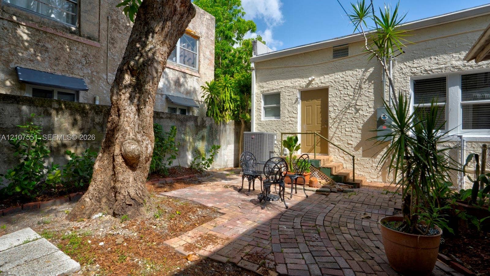 1676 SW 11th Street, Miami, Miami, FL 33135 Private outdoor courtyard featuring decorative brick pavers, stucco exterior wall finishes, and a mature shade tree