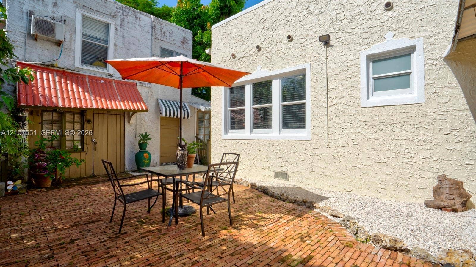 1676 SW 11th Street, Miami, Miami, FL 33135 Enclosed courtyard featuring a red brick patio, textured stucco exterior walls, multi-pane windows, and a terracotta-style awning