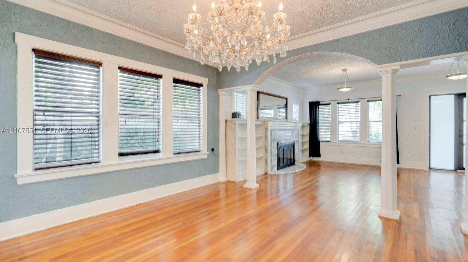 1676 SW 11th Street, Miami, Miami, FL 33135 Living area featuring wood-finish flooring, a multi-light crystal chandelier, a fireplace with a stone-surround mantel, built-in shelving, and architectural columns