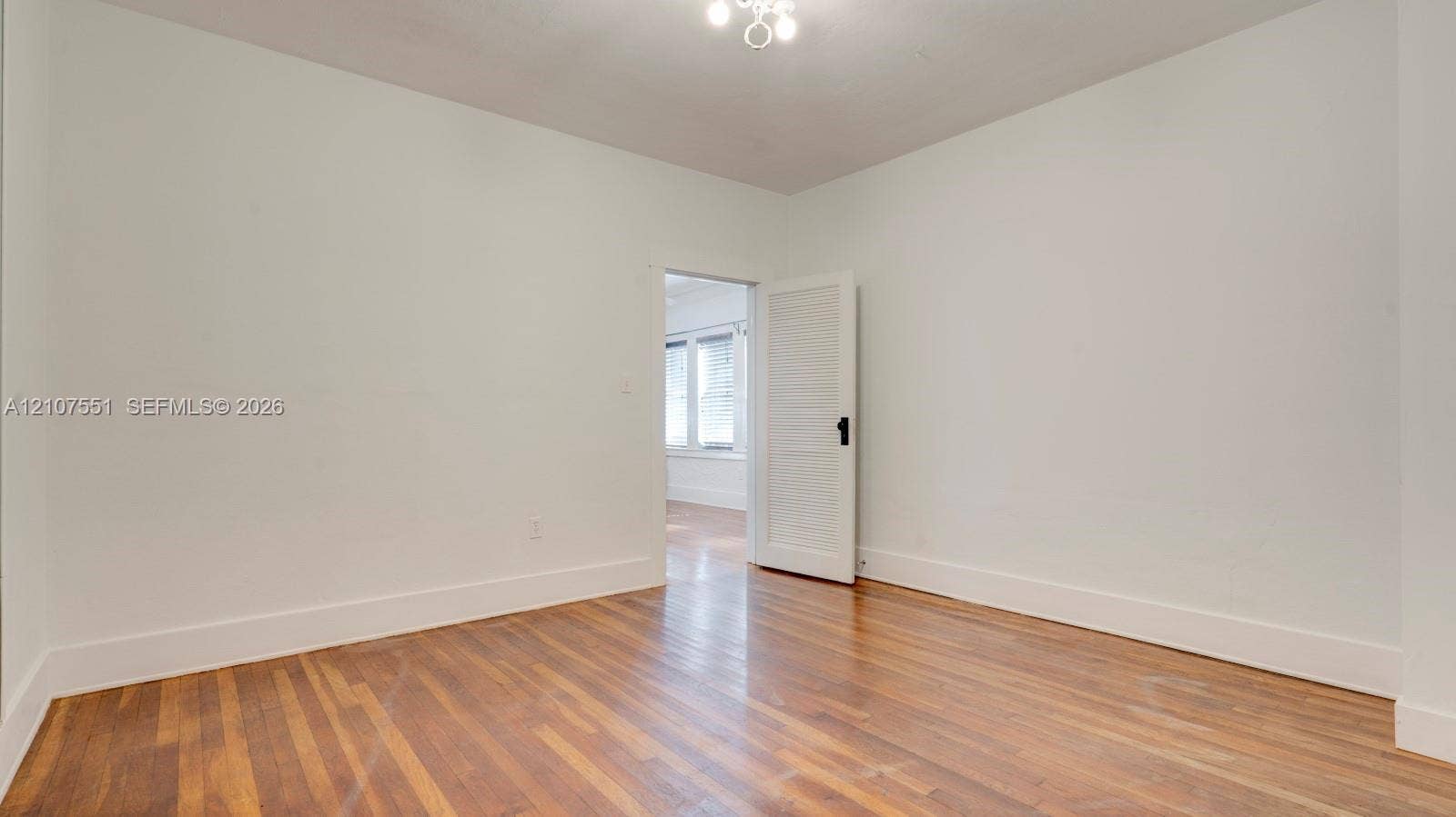 1676 SW 11th Street, Miami, Miami, FL 33135 Room interior featuring wood-finish flooring, a white five-panel interior door with a black hardware set, and a ceiling-mounted light fixture