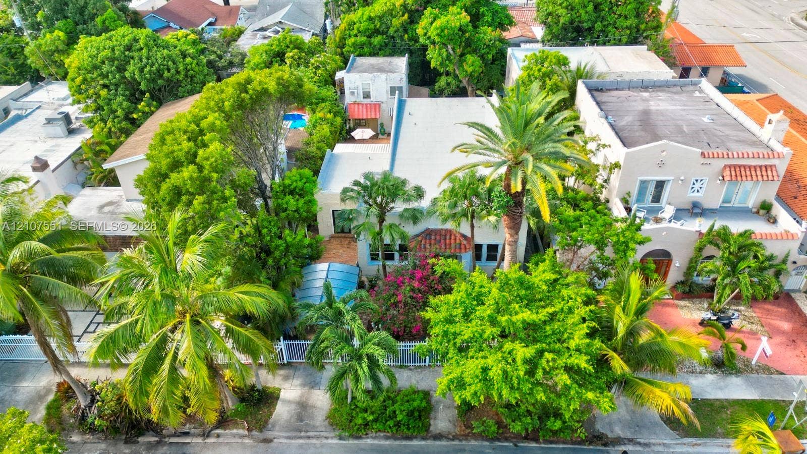 1676 SW 11th Street, Miami, Miami, FL 33135 Aerial perspective of a property featuring mature tropical landscaping, palm trees, a concrete-surfaced driveway, and a fenced perimeter