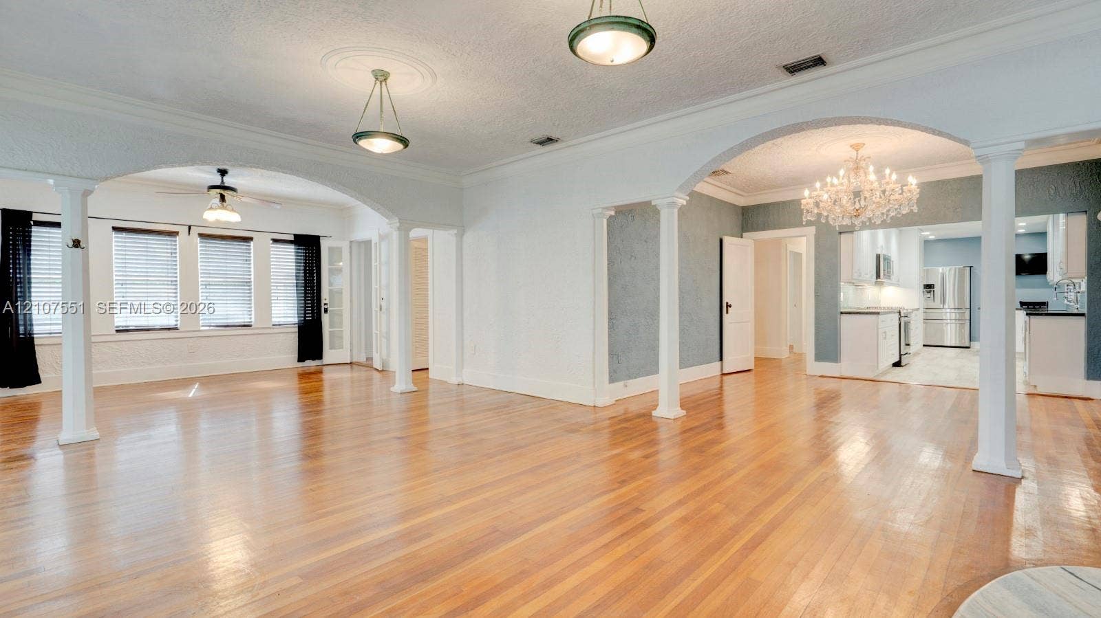 1676 SW 11th Street, Miami, Miami, FL 33135 Open-concept living space featuring wood-finish flooring, decorative architectural columns, arched entryways, and crystal-style chandelier lighting