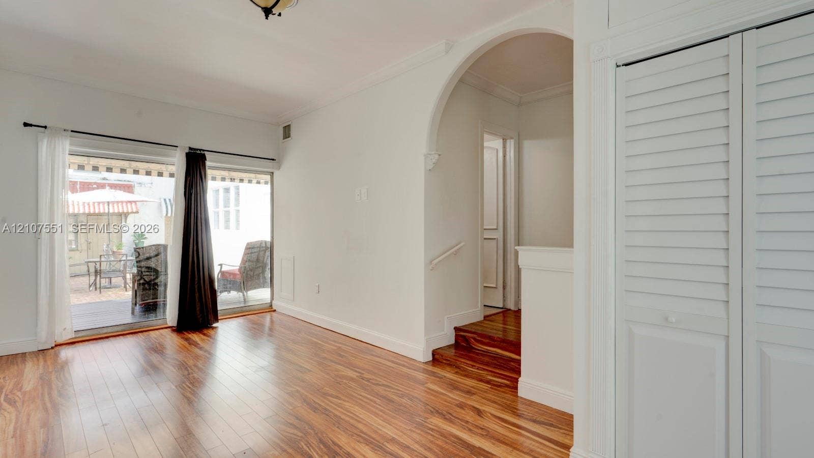 1676 SW 11th Street, Miami, Miami, FL 33135 Interior space featuring wood-finish flooring, a decorative architectural archway, floor-to-ceiling sliding glass doors, louvered closet doors, and hardwood-surfaced stairs