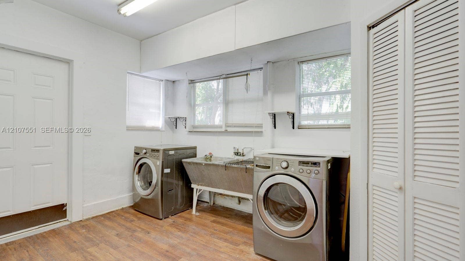1676 SW 11th Street, Miami, Miami, FL 33135 Laundry area featuring wood-finish flooring, a stainless steel utility sink, and louvered closet doors