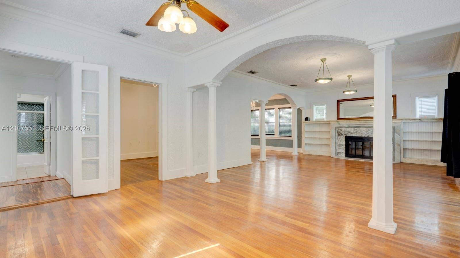 1676 SW 11th Street, Miami, Miami, FL 33135 Interior space featuring architectural columns, arched entryways, wood-finish flooring, a fireplace with stone surround, and built-in shelving