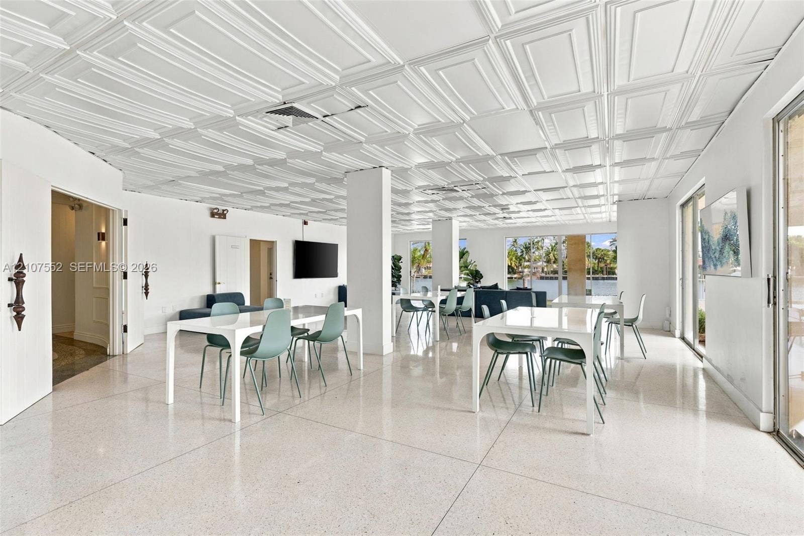 Expansive open-concept room featuring decorative coffered ceiling panels, polished stone flooring, and floor-to-ceiling glass sliding doors