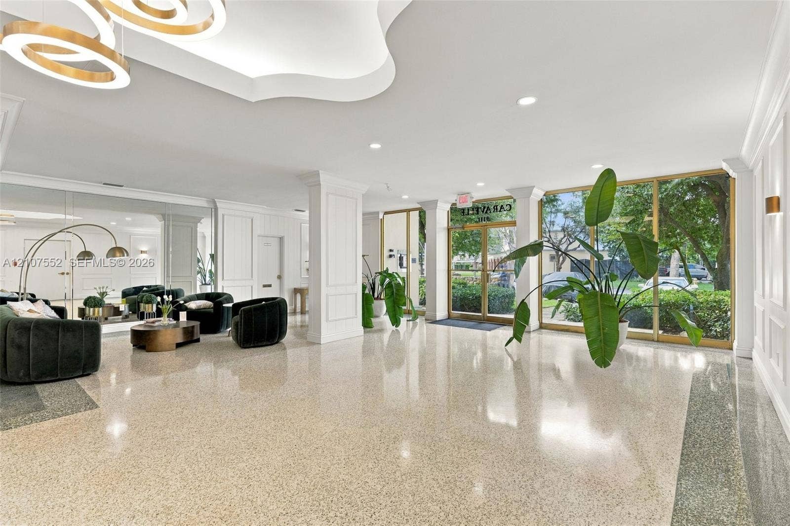 Spacious lobby featuring polished stone flooring, intricate crown molding, architectural columns, a modern multi-tiered chandelier, and floor-to-ceiling glass windows with metal framing