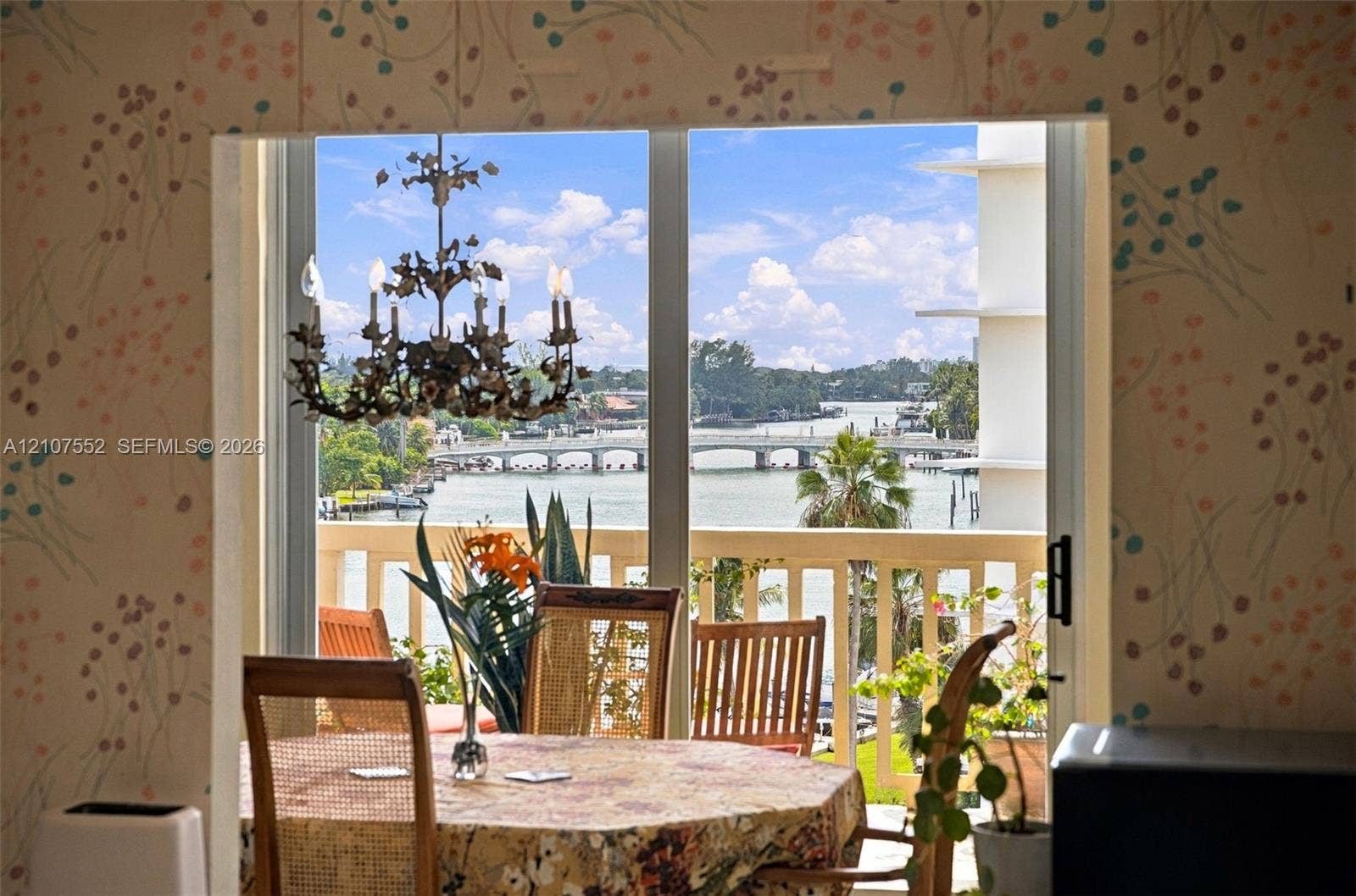 Floor-to-ceiling sliding glass door, decorative metal chandelier, and exterior balcony featuring a balustrade railing with water and bridge scenery