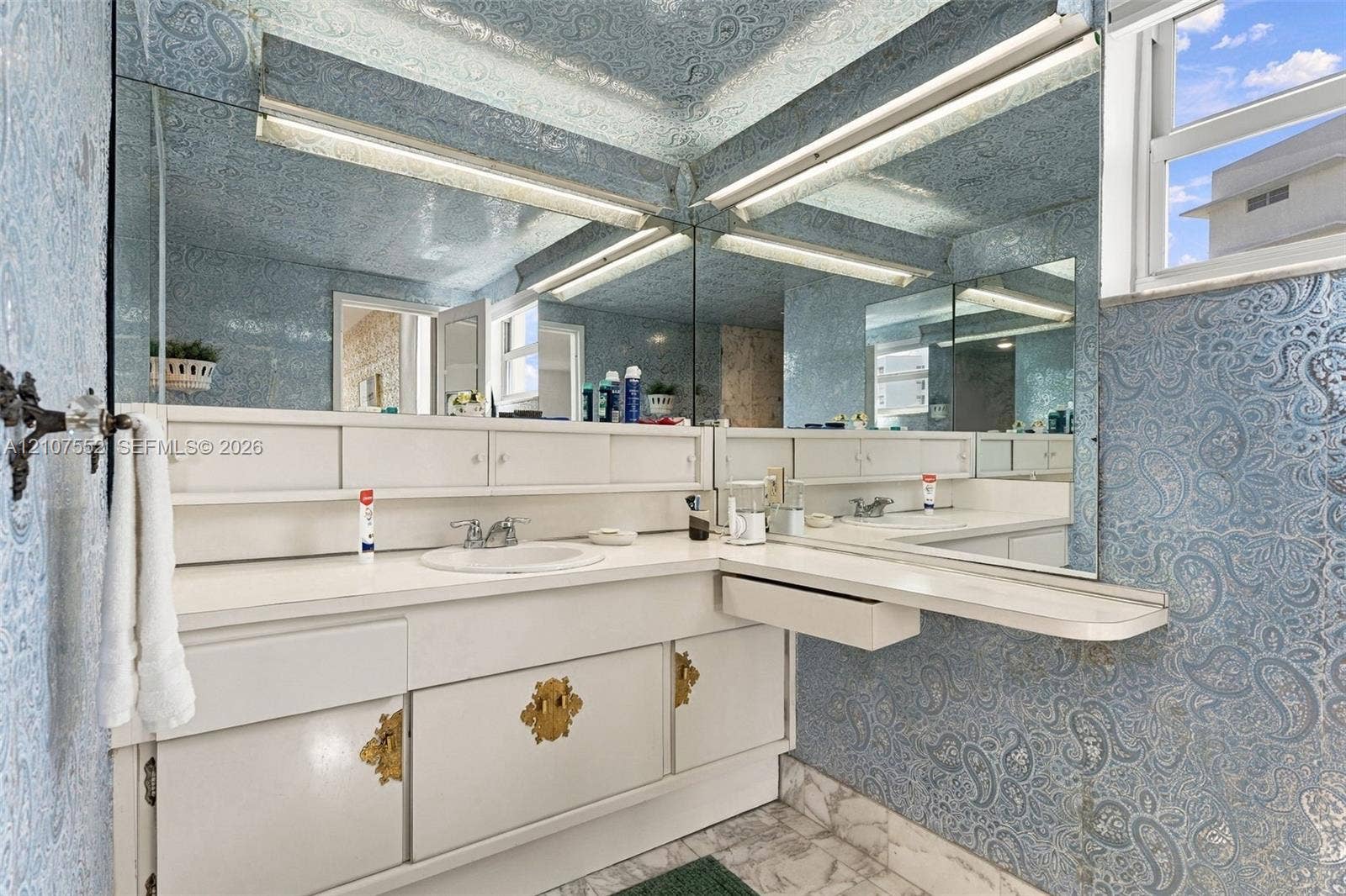 Built-in white vanity with integrated cabinetry, polished gold-toned hardware, solid-surface countertop, circular drop-in sink, and expansive wall-to-wall mirror
