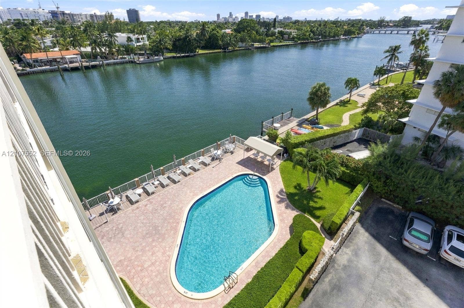Waterfront swimming pool with paver patio, manicured landscaping, and bulkhead shoreline