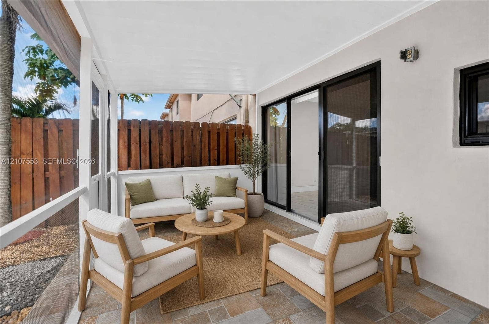 7336 SW 26th Court, #51, Davie, Davie, FL 33314 Screened-in patio featuring stone-tile flooring, a white-finished ceiling, and sliding glass doors with black frames, enclosed by a wood-plank privacy fence