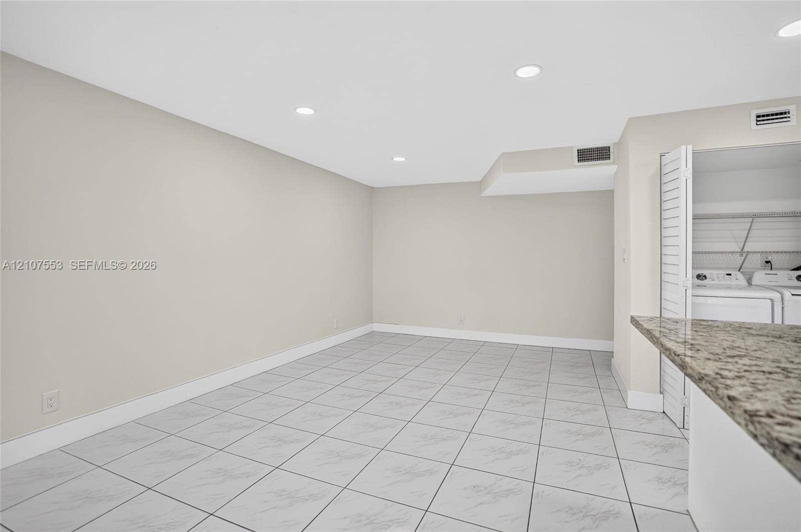 7336 SW 26th Court, #51, Davie, Davie, FL 33314 Neutral-toned interior space featuring light-colored tile flooring, recessed lighting, and a built-in stone-top counter with an integrated utility area behind louvered doors