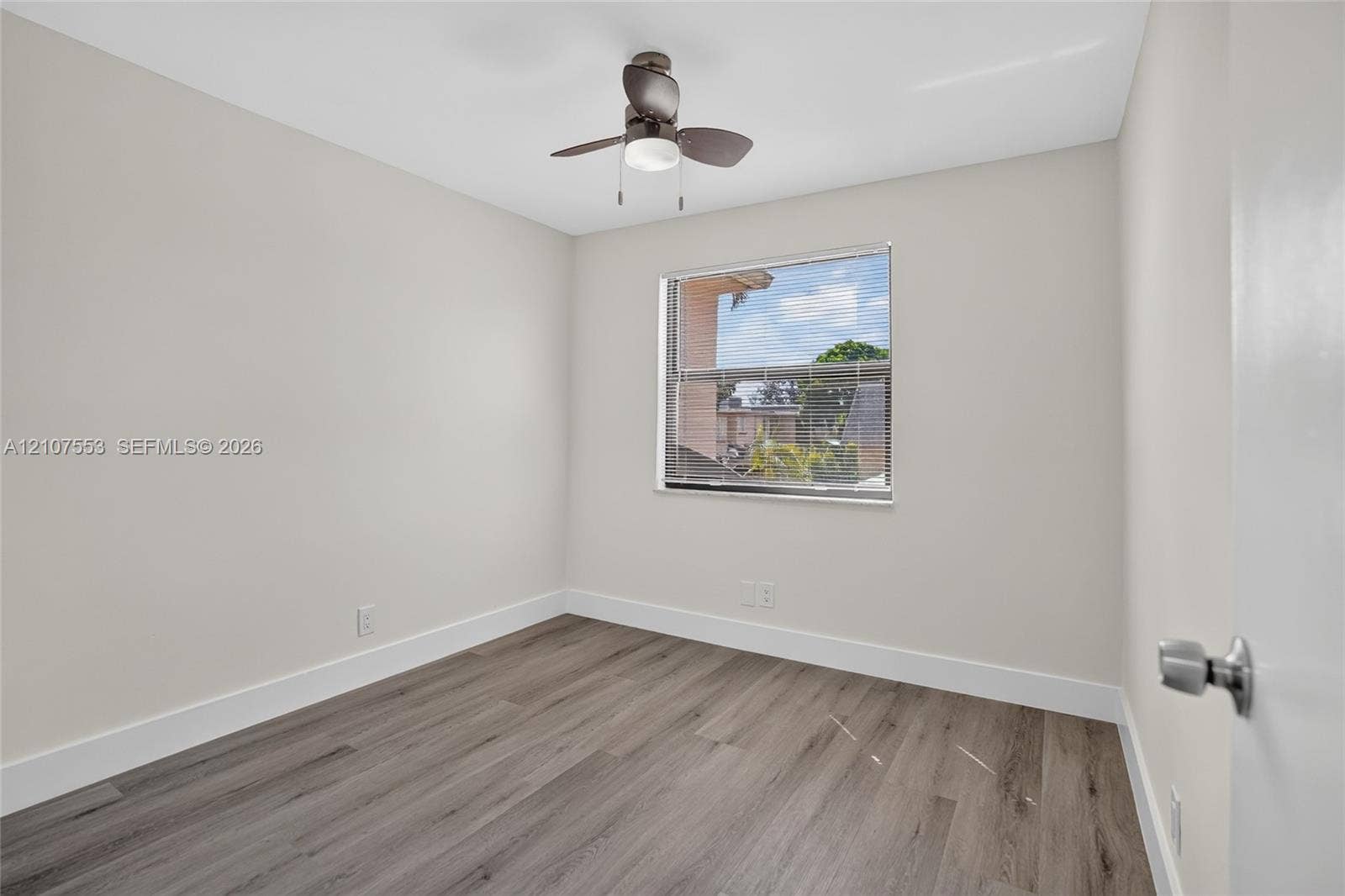 7336 SW 26th Court, #51, Davie, Davie, FL 33314 Neutral-toned interior room featuring wood-finish flooring, a ceiling fan with integrated light fixture, and a window with horizontal blinds