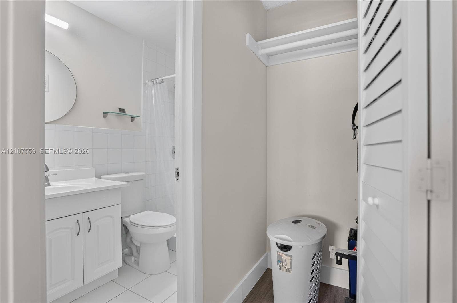 7336 SW 26th Court, #51, Davie, Davie, FL 33314 Bathroom featuring a white vanity cabinet, tiled shower surround, wall-mounted circular mirror, and louvered closet doors with integrated shelving