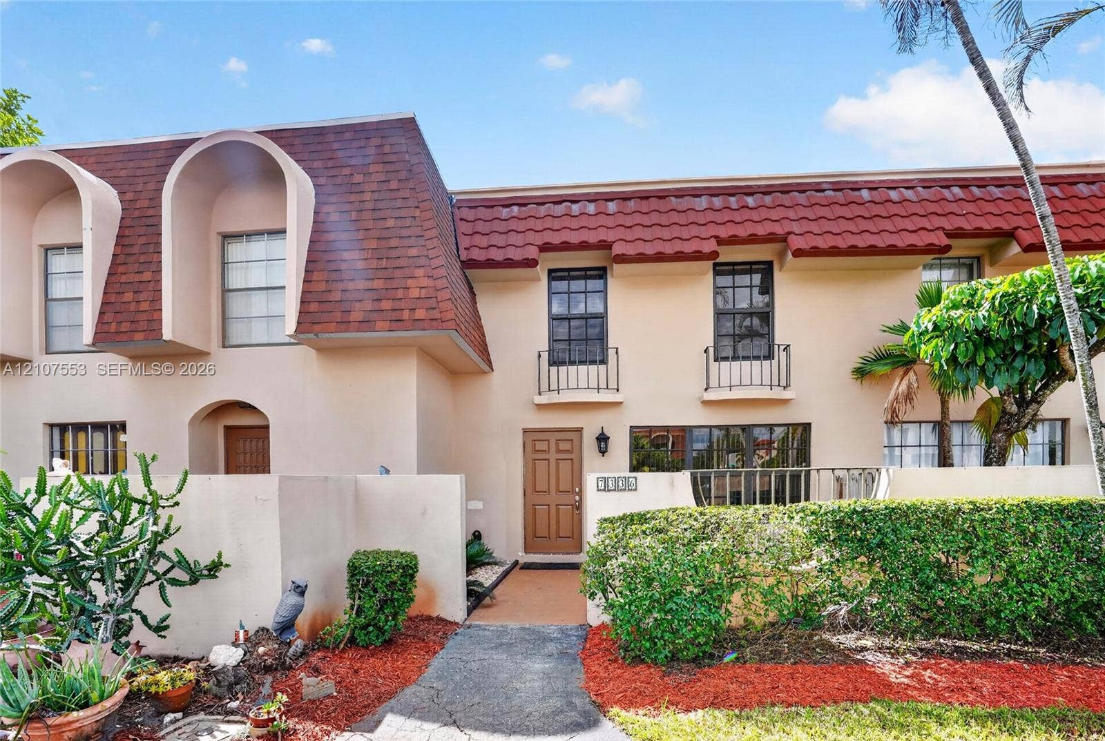 7336 SW 26th Court, #51, Davie, Davie, FL 33314 Exterior facade featuring a mansard roofline with patterned shingle detailing, terracotta-colored roof tiles, wrought-iron balcony railings, and a stucco finish