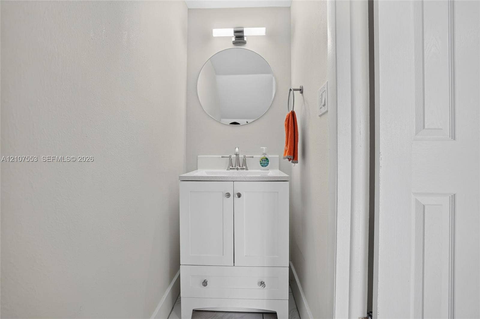 7336 SW 26th Court, #51, Davie, Davie, FL 33314 White vanity with lower storage drawer, integrated basin, brushed nickel hardware, circular wall-mounted mirror, and horizontal LED light fixture