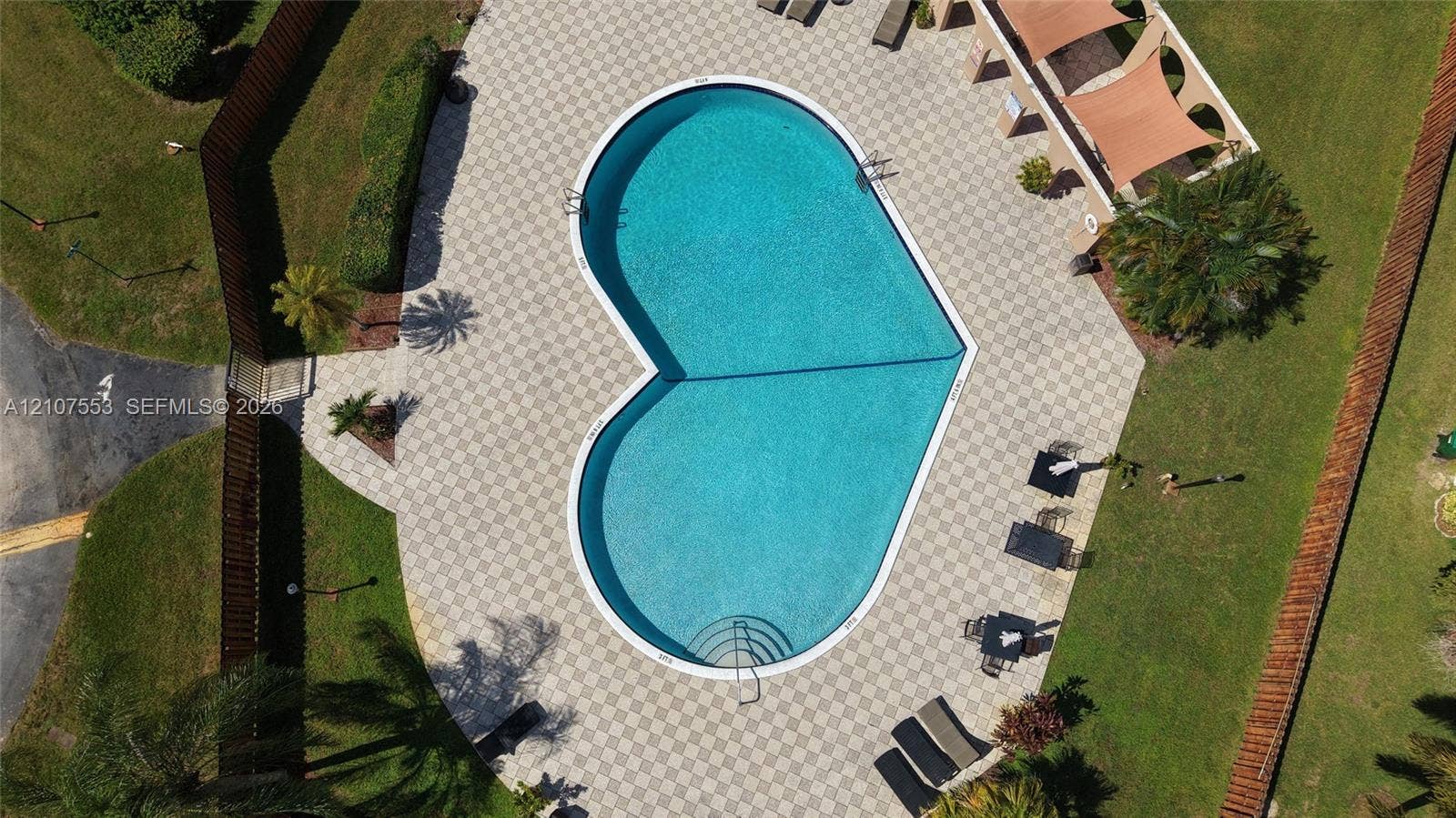 7336 SW 26th Court, #51, Davie, Davie, FL 33314 Heart-shaped swimming pool with built-in steps, surrounded by a paved patio, manicured lawn, and wooden perimeter fencing
