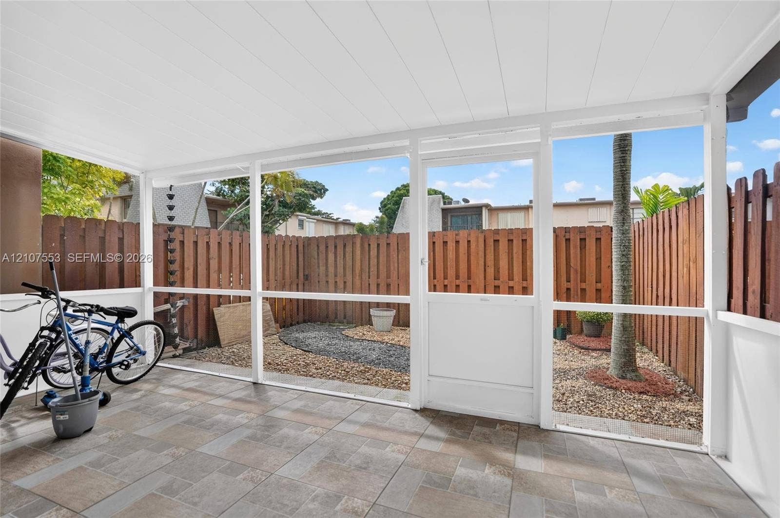 7336 SW 26th Court, #51, Davie, Davie, FL 33314 Screened-in patio with tile flooring, a white paneled ceiling, and a wooden privacy fence enclosing a gravel courtyard