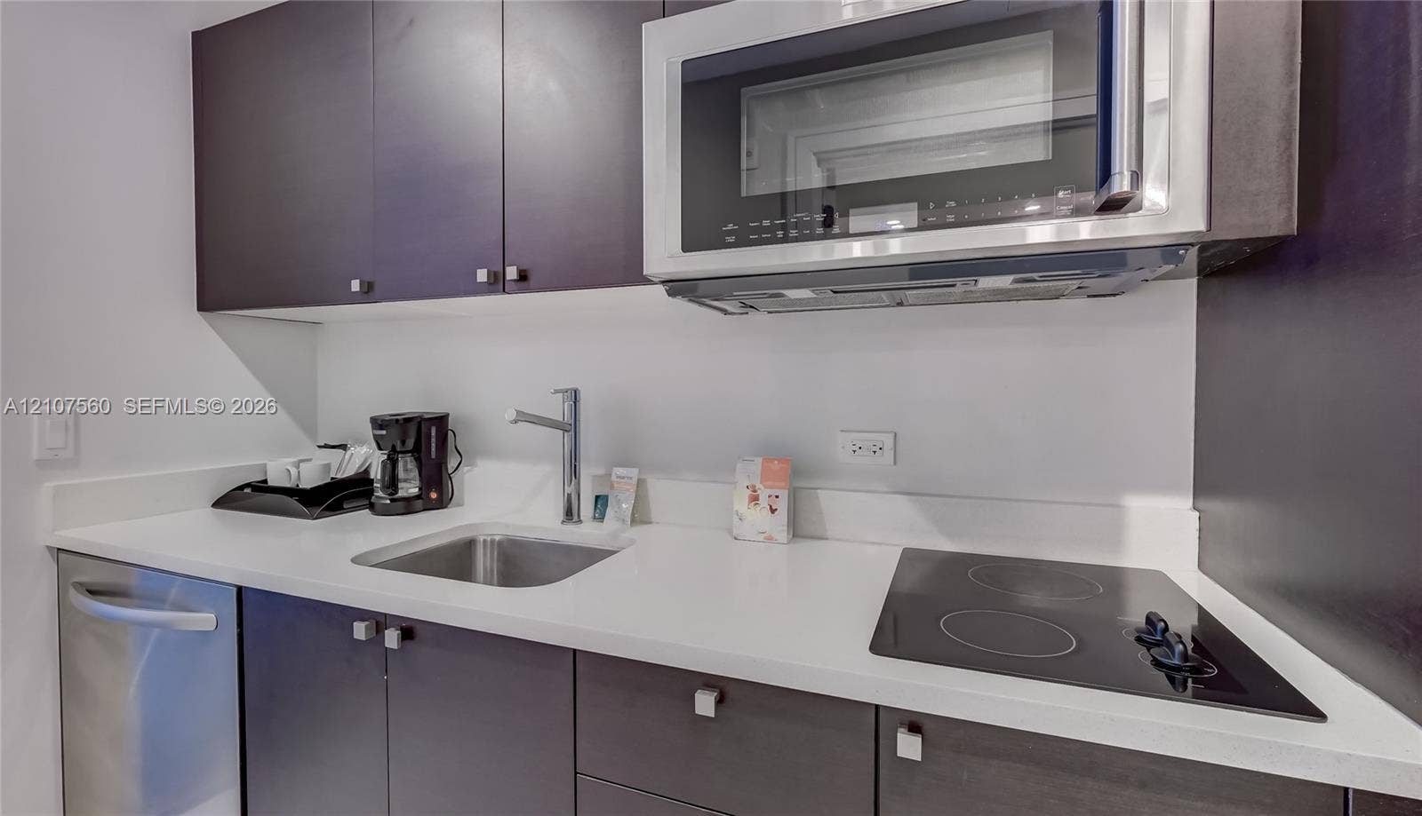 5300 NW 87th Avenue, #407, Doral, FL 33178 Kitchen area featuring dark cabinetry, solid surface countertops, stainless steel undermount sink, built-in microwave, and electric cooktop