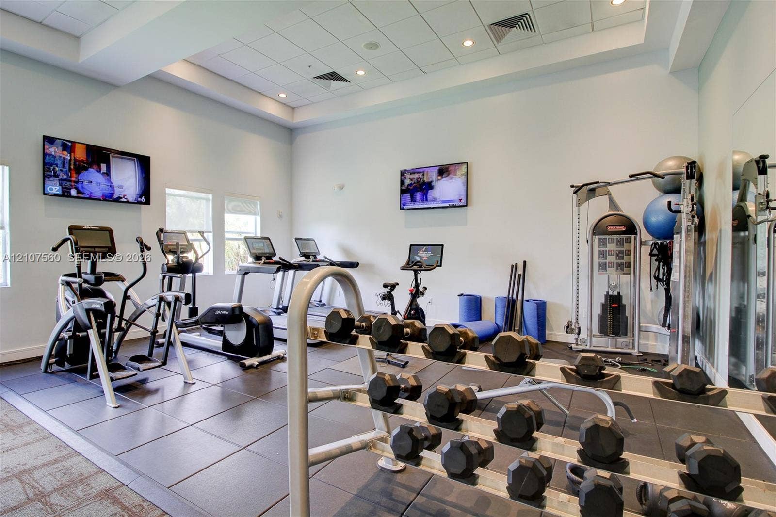 5300 NW 87th Avenue, #407, Doral, FL 33178 Fitness center featuring recessed tray ceilings, large-format tile flooring, wall-mounted televisions, and mirrored wall surfaces
