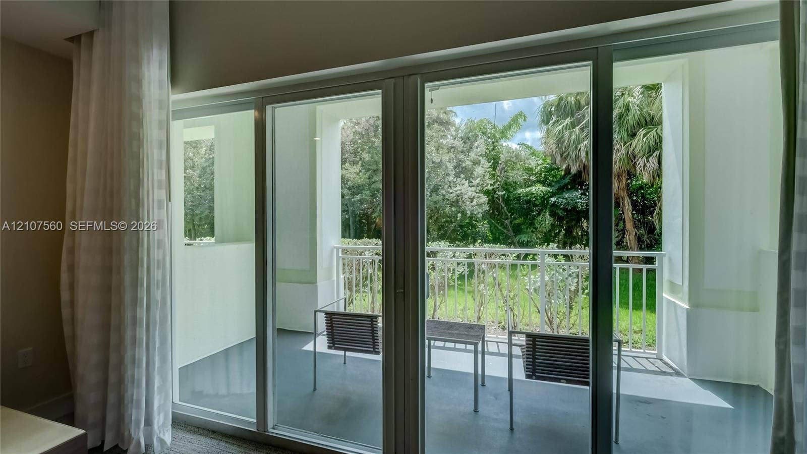 5300 NW 87th Avenue, #407, Doral, FL 33178 Floor-to-ceiling sliding glass doors opening to a covered balcony with white metal railings and greenery backdrop