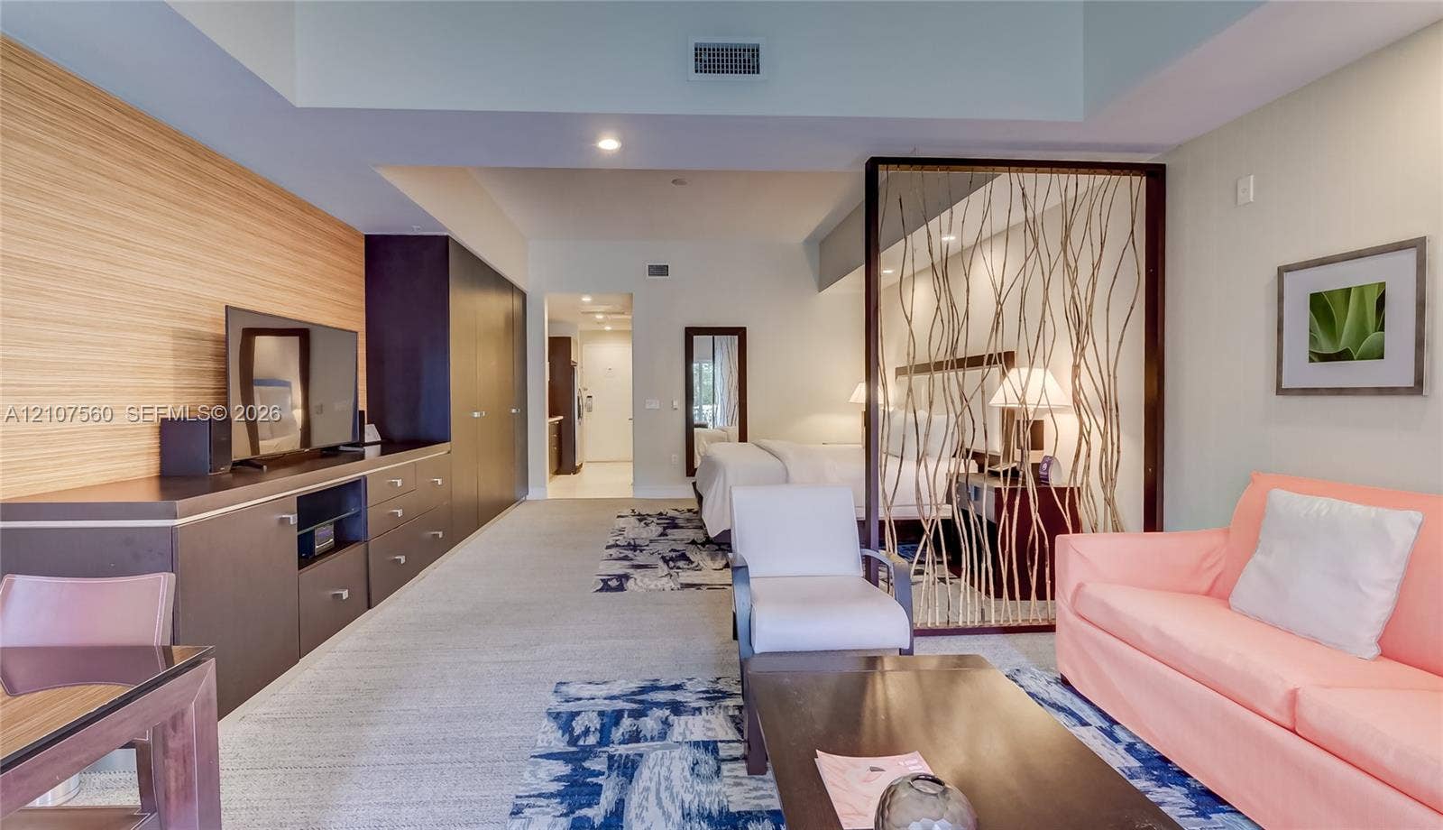 5300 NW 87th Avenue, #407, Doral, FL 33178 Open-concept interior featuring horizontal wood-slatted accent wall, built-in cabinetry with flat-panel doors, decorative branch-pattern room divider, recessed lighting, and wall-to-wall carpeting