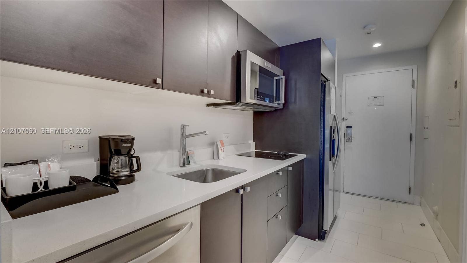 5300 NW 87th Avenue, #407, Doral, FL 33178 Kitchenette featuring flat-panel cabinetry, a solid-surface countertop, stainless steel sink with a high-arch faucet, a built-in microwave, and an integrated cooktop