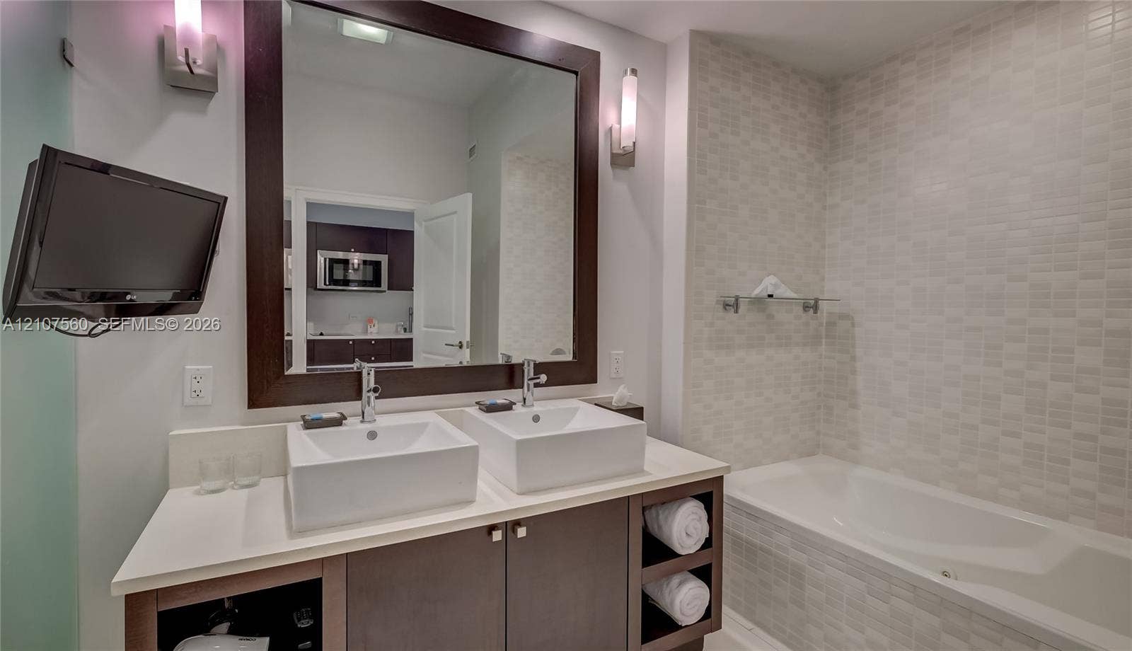 5300 NW 87th Avenue, #407, Doral, FL 33178 Double vanity featuring square vessel sinks, white countertop, dark-finish cabinetry with open shelving, and a large framed mirror with integrated wall-mounted lighting