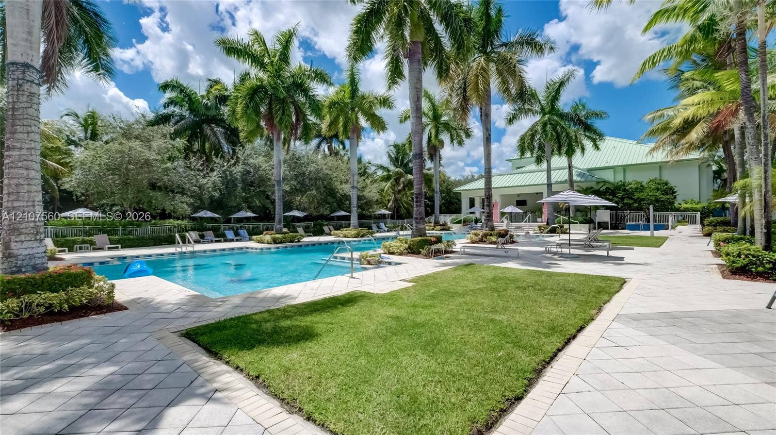 5300 NW 87th Avenue, #407, Doral, FL 33178 Outdoor swimming pool featuring a paved deck, manicured lawn, palm trees, and structural shaded areas
