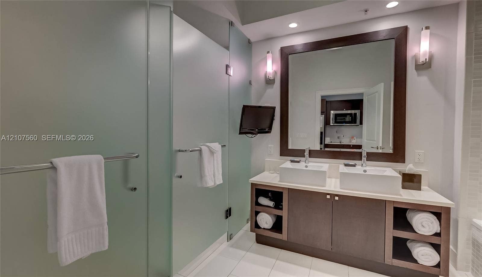 5300 NW 87th Avenue, #407, Doral, FL 33178 Double vanity featuring rectangular vessel sinks, light-toned stone-surface countertop, dark wood-finish cabinetry with open shelving, large wall-mounted mirror with wood frame, and frosted glass shower enclosure
