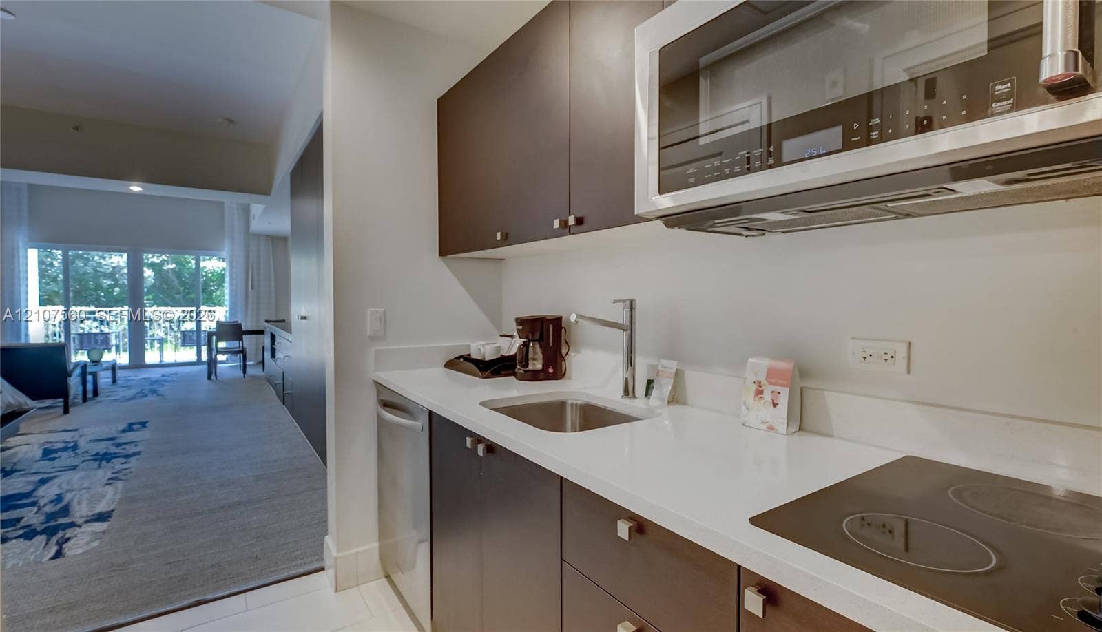 5300 NW 87th Avenue, #407, Doral, FL 33178 Kitchenette featuring dark-finish cabinetry, solid-surface countertops, a stainless steel undermount sink with a gooseneck faucet, an integrated cooktop, and a stainless steel over-the-range microwave
