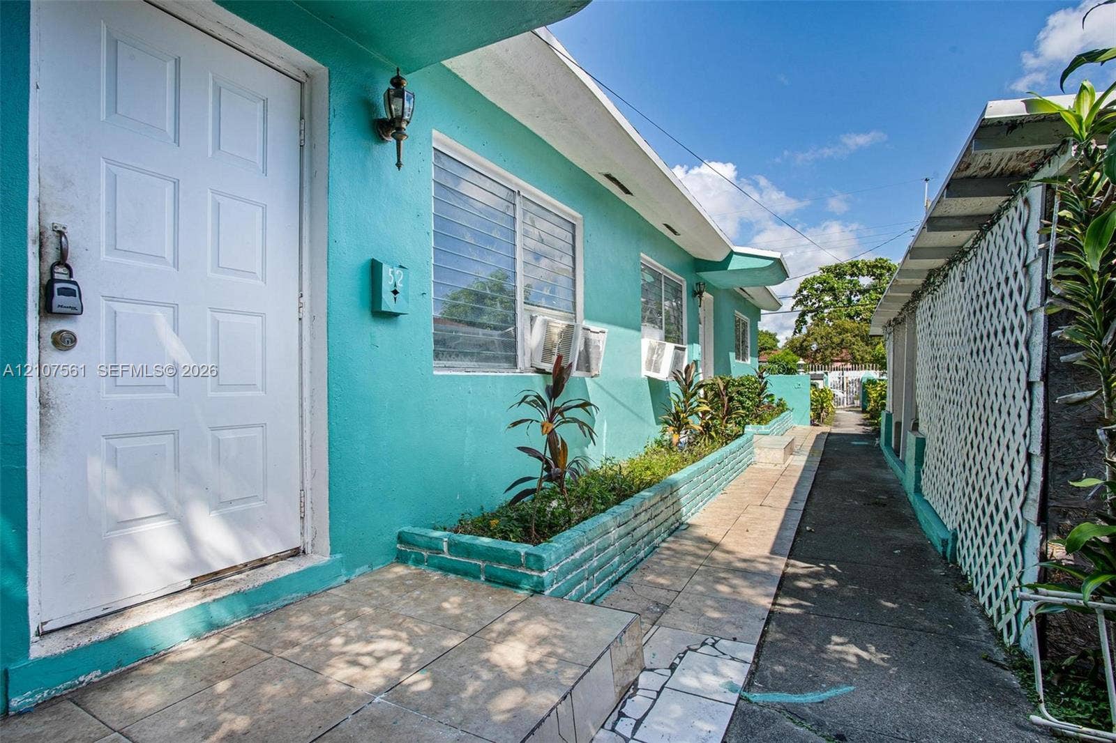 50 NW 69th Street, Miami, FL 33150 Exterior facade featuring a painted masonry finish, raised brick planter, tile-surfaced entryway, and white lattice fencing