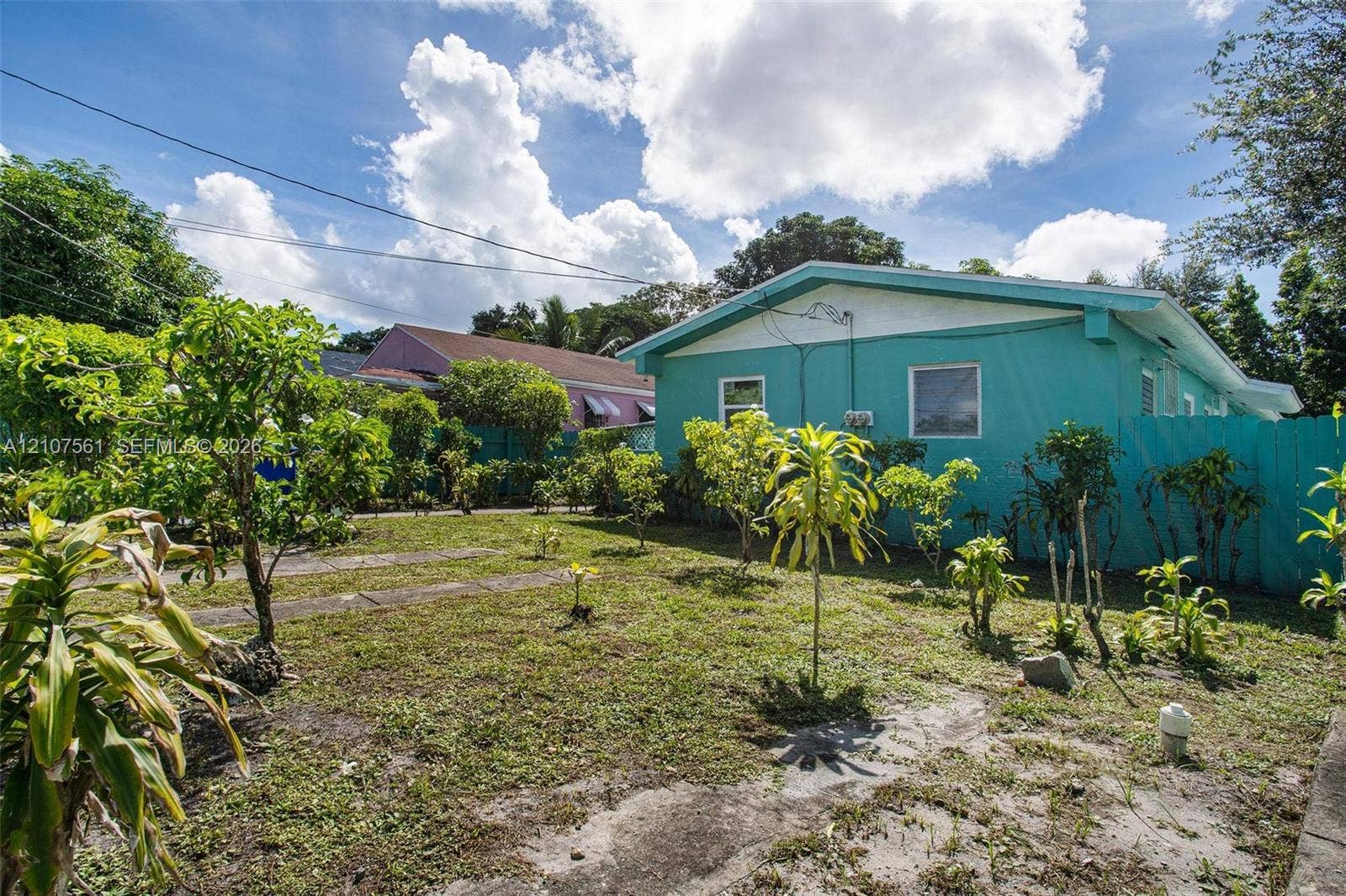50 NW 69th Street, Miami, FL 33150 Exterior side yard featuring a concrete path, perimeter wood fencing, and mature landscaping